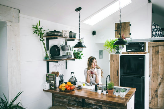 A woman enjoying tea in a cozy, modern kitchen with a compact black refrigerator. Ideal setup for small spaces and stylish appliance solutions.