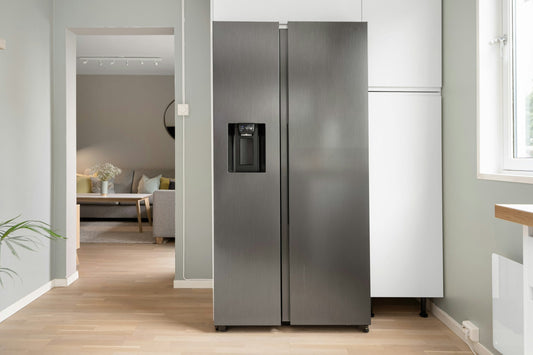 Modern side-by-side stainless steel refrigerator in a minimalist Canadian kitchen with light wood flooring and soft grey walls.